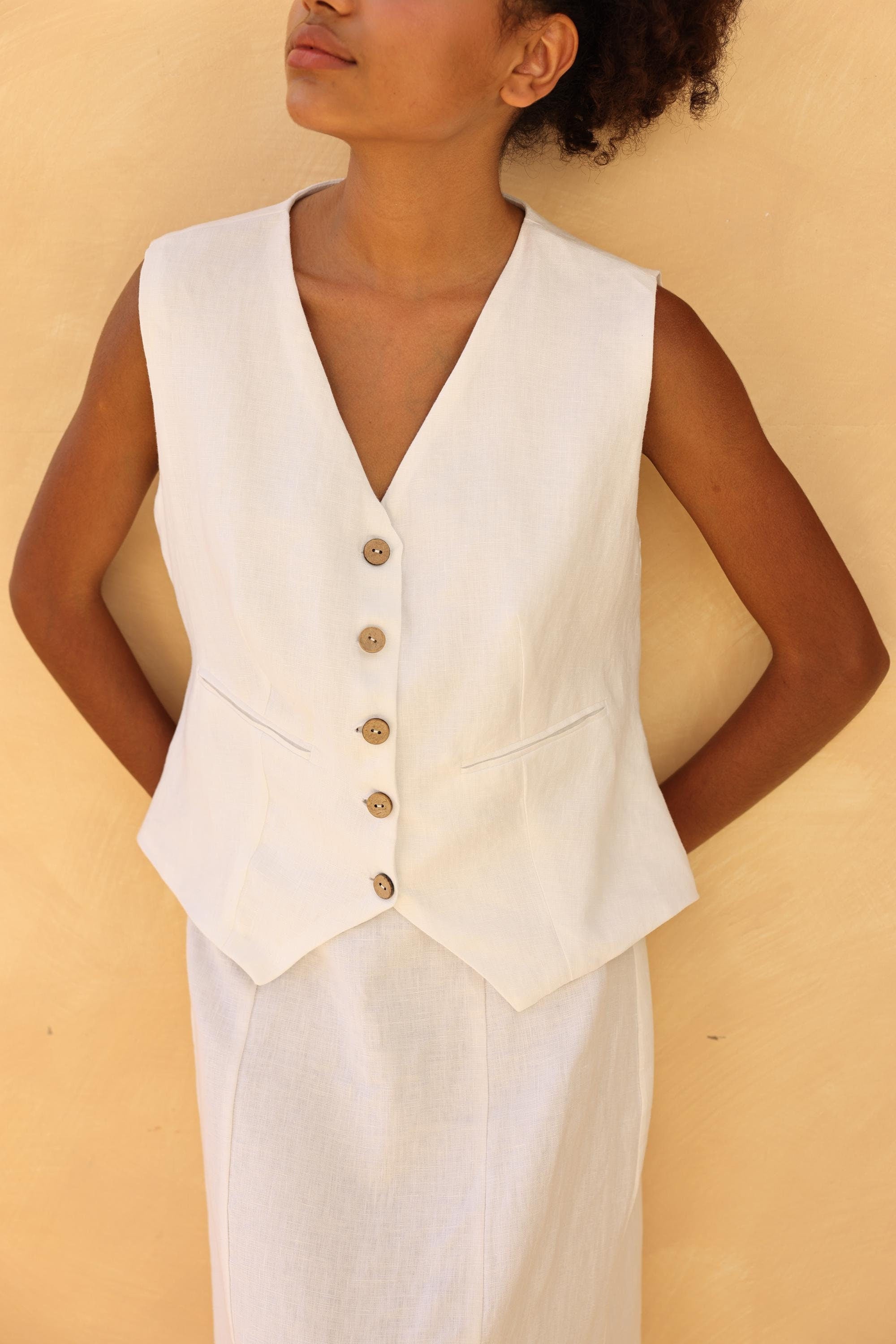 Woman wearing a white vest with buttons against a beige background