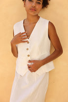 Woman wearing a white sleeveless blazer with buttons against a beige background