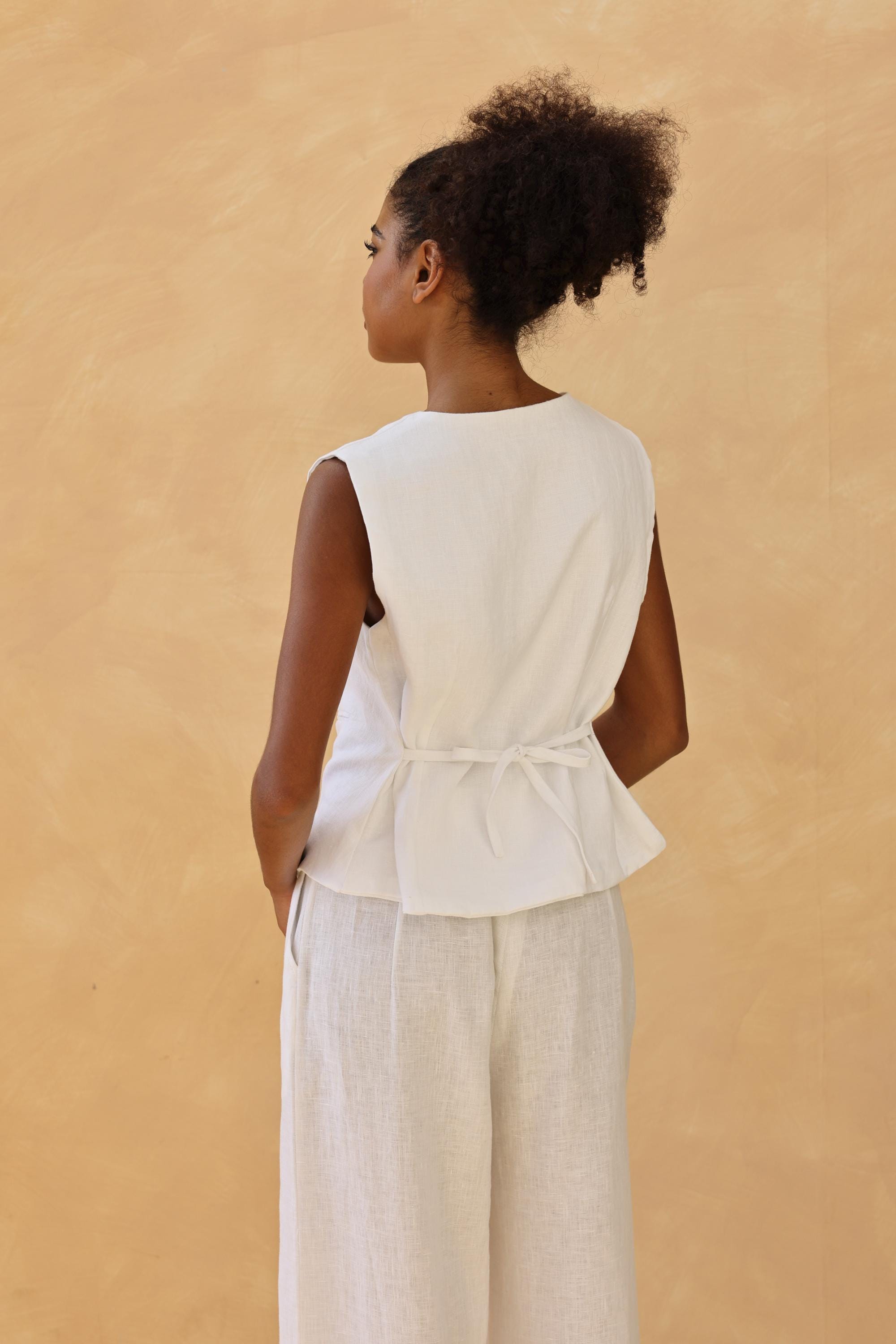 Woman wearing a white sleeveless top and light-colored pants against a beige background