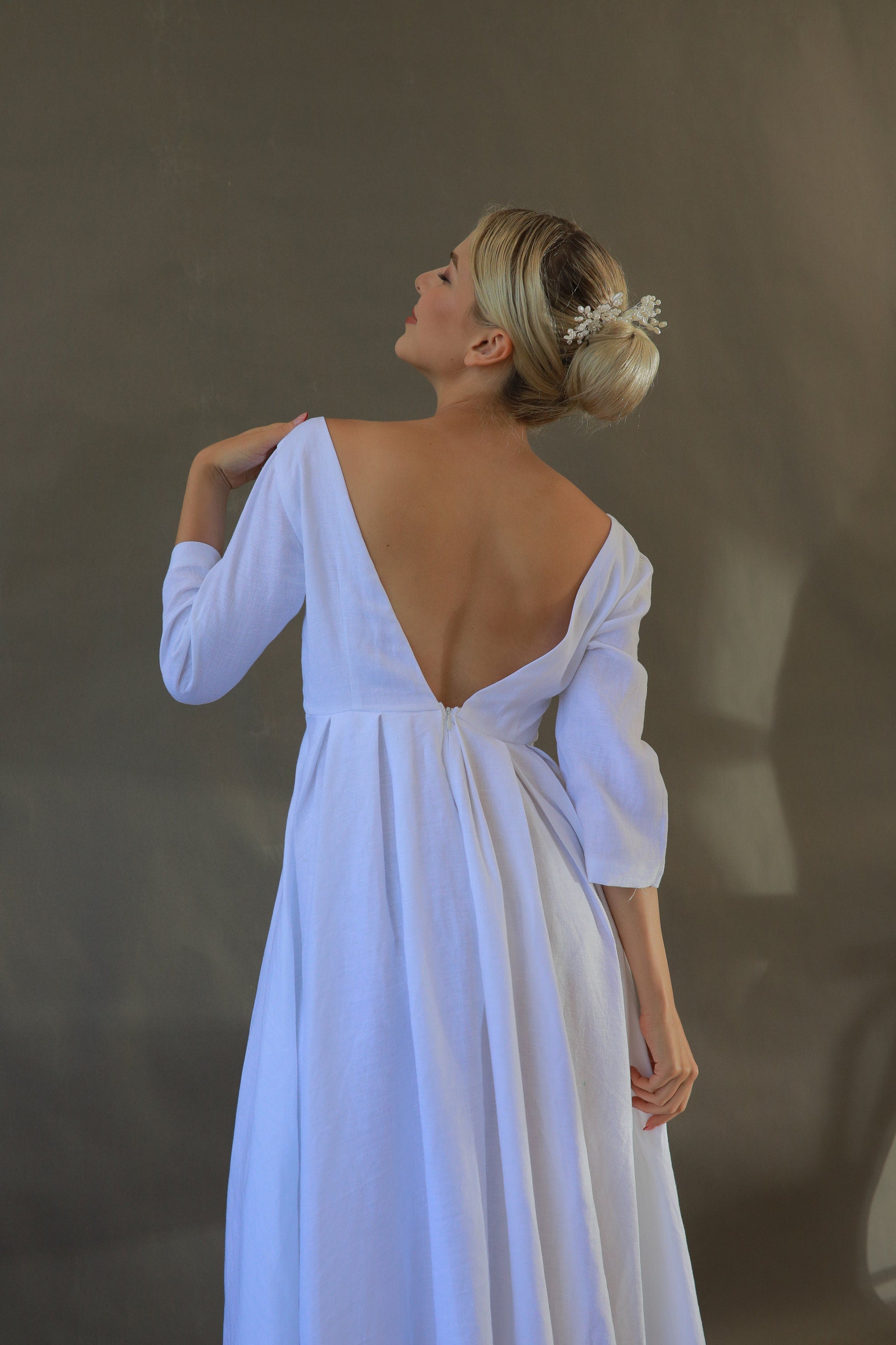 Woman wearing a white dress with a deep backless design against a neutral background