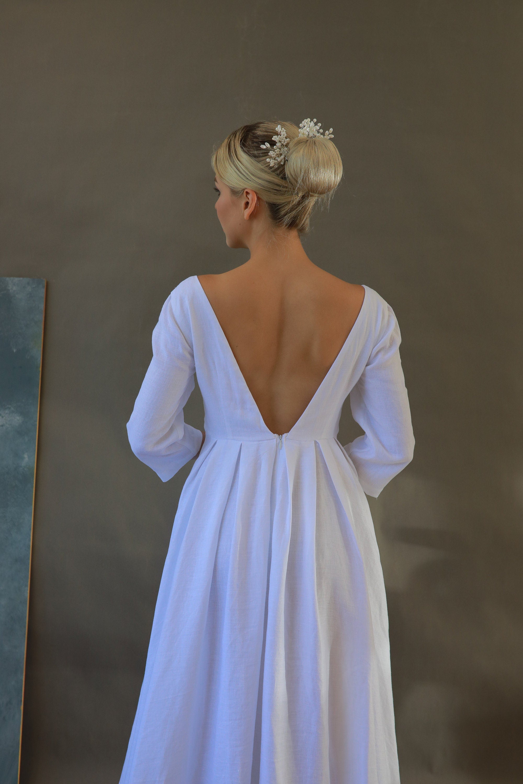Woman wearing a white wedding dress with a low back and 3/4 sleeves against a plain background
