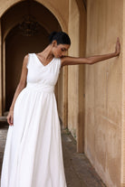 Woman in a white dress standing against a beige wall with an archway.
