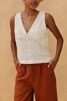 Person wearing a sleeveless top and rust-colored pants against a beige background