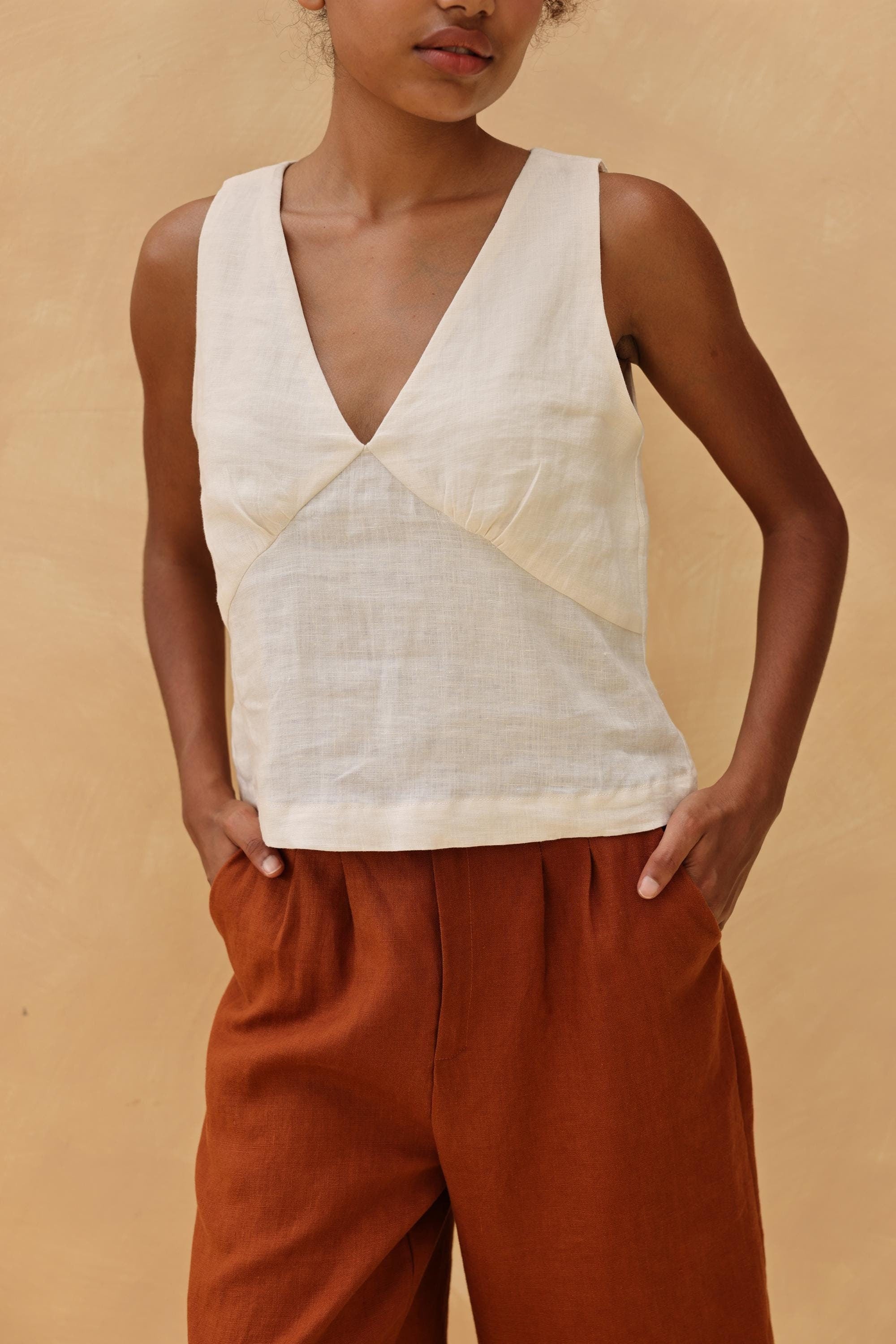 Person wearing a sleeveless top and rust-colored pants against a beige background