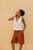 Woman wearing a sleeveless top and brown shorts against a beige background