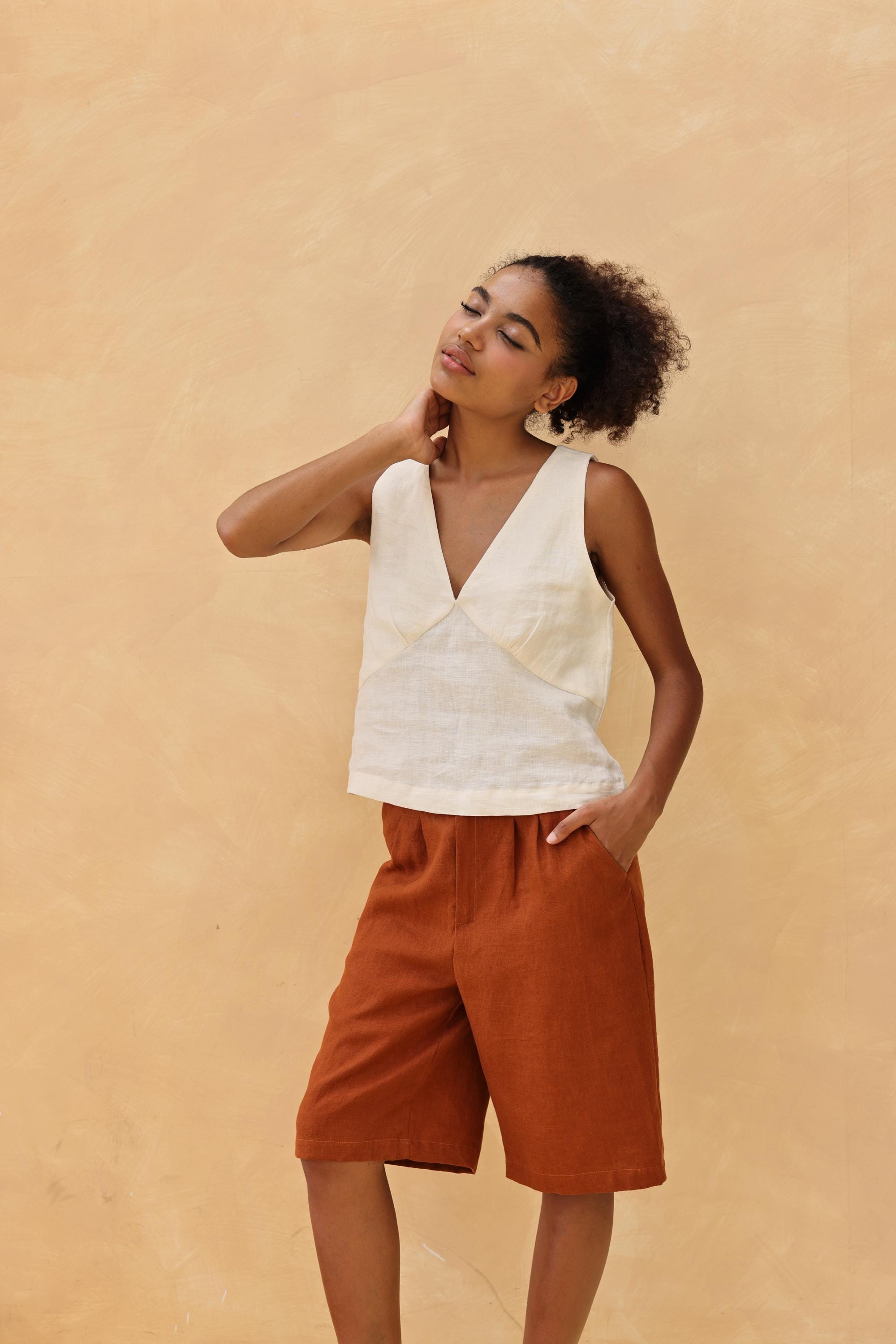 Woman wearing a sleeveless top and brown shorts against a beige background