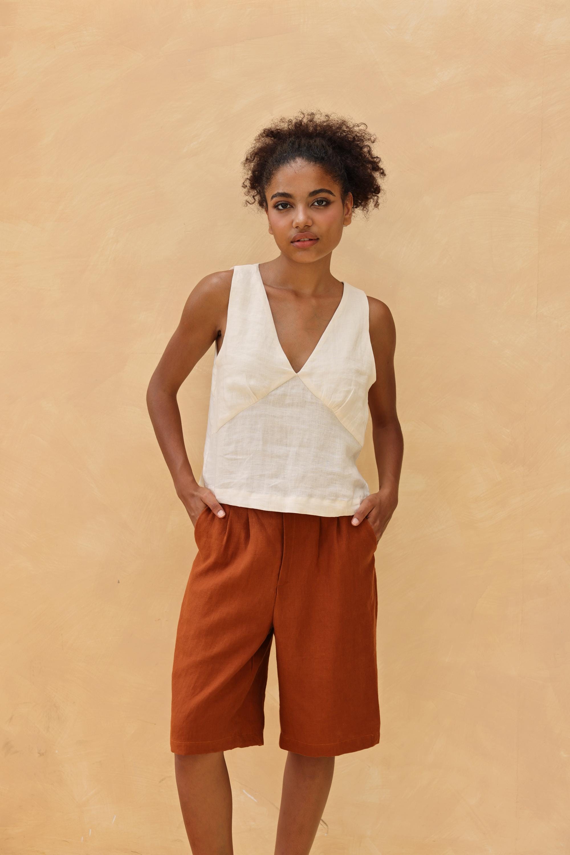 Woman wearing a sleeveless top and brown shorts against a beige background