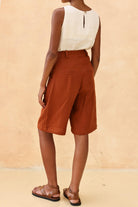 Person wearing a sleeveless top and brown shorts against a beige background