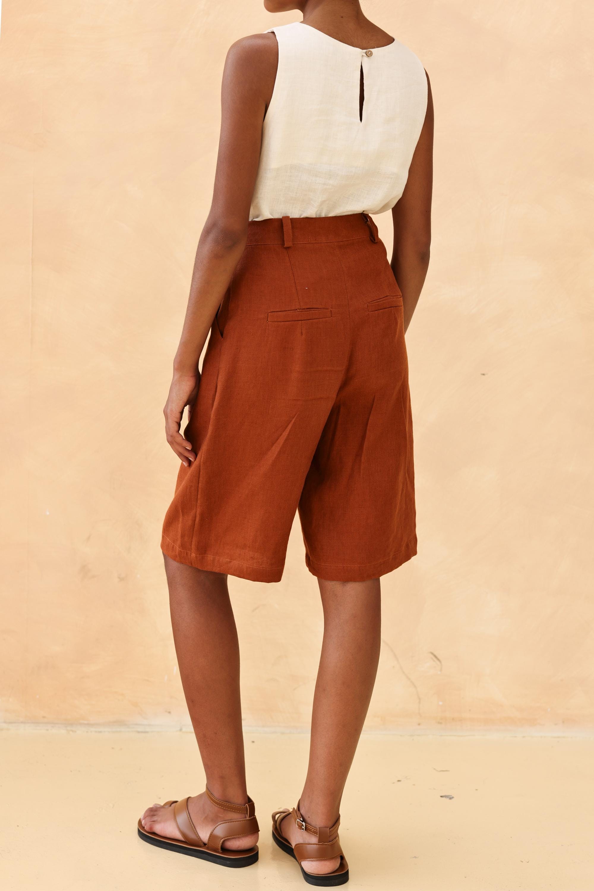 Person wearing a sleeveless top and brown shorts against a beige background