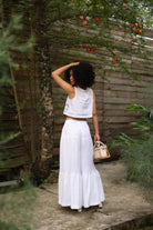 Woman in a white outfit standing in a garden with wooden walls and plants.