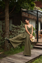 Woman in a green outfit standing on a wooden path with a building and trees in the background