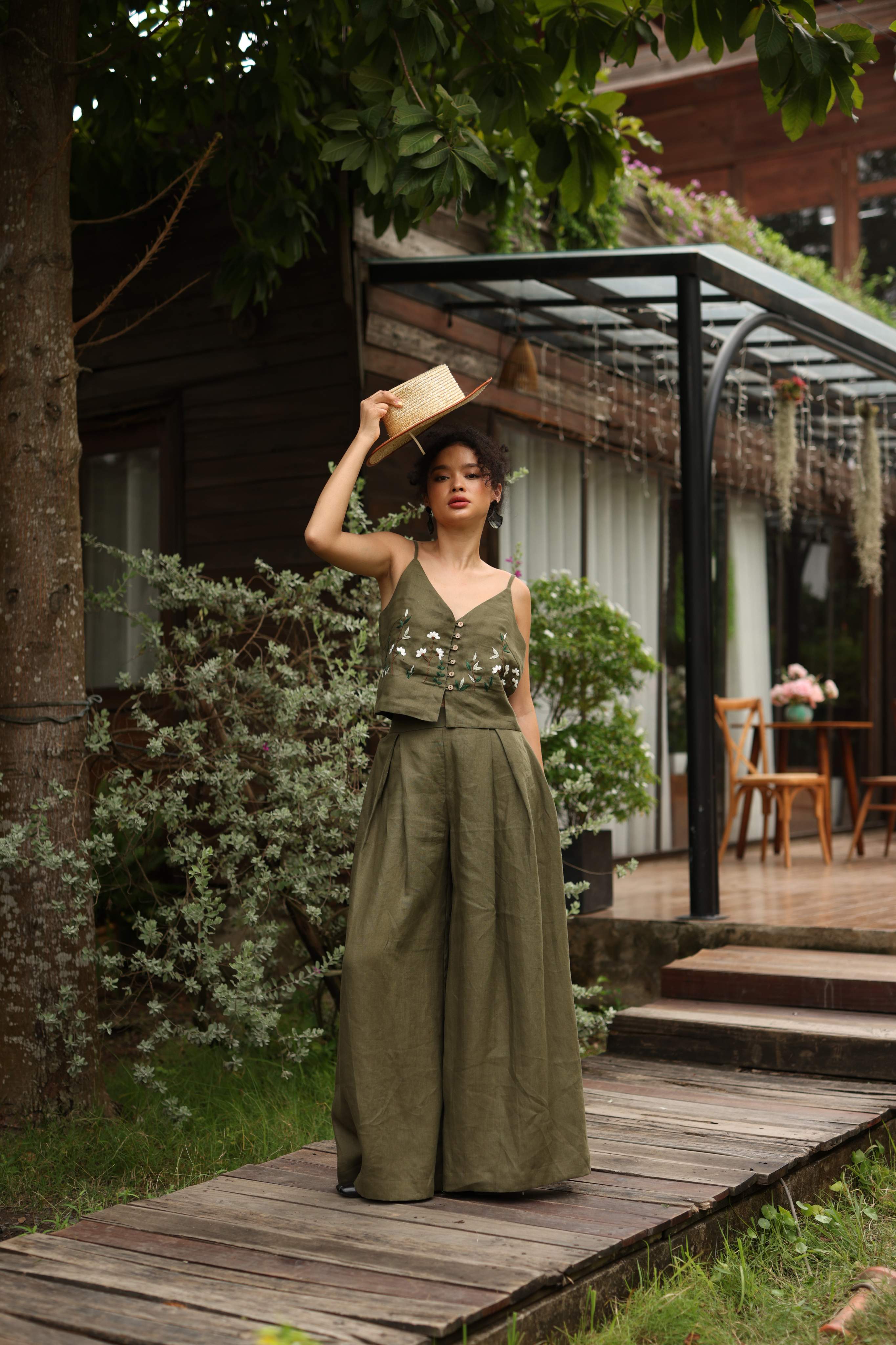 Woman in a green outfit standing on a wooden path with a rustic background