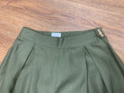 Green pleated pants with button details on a wooden surface