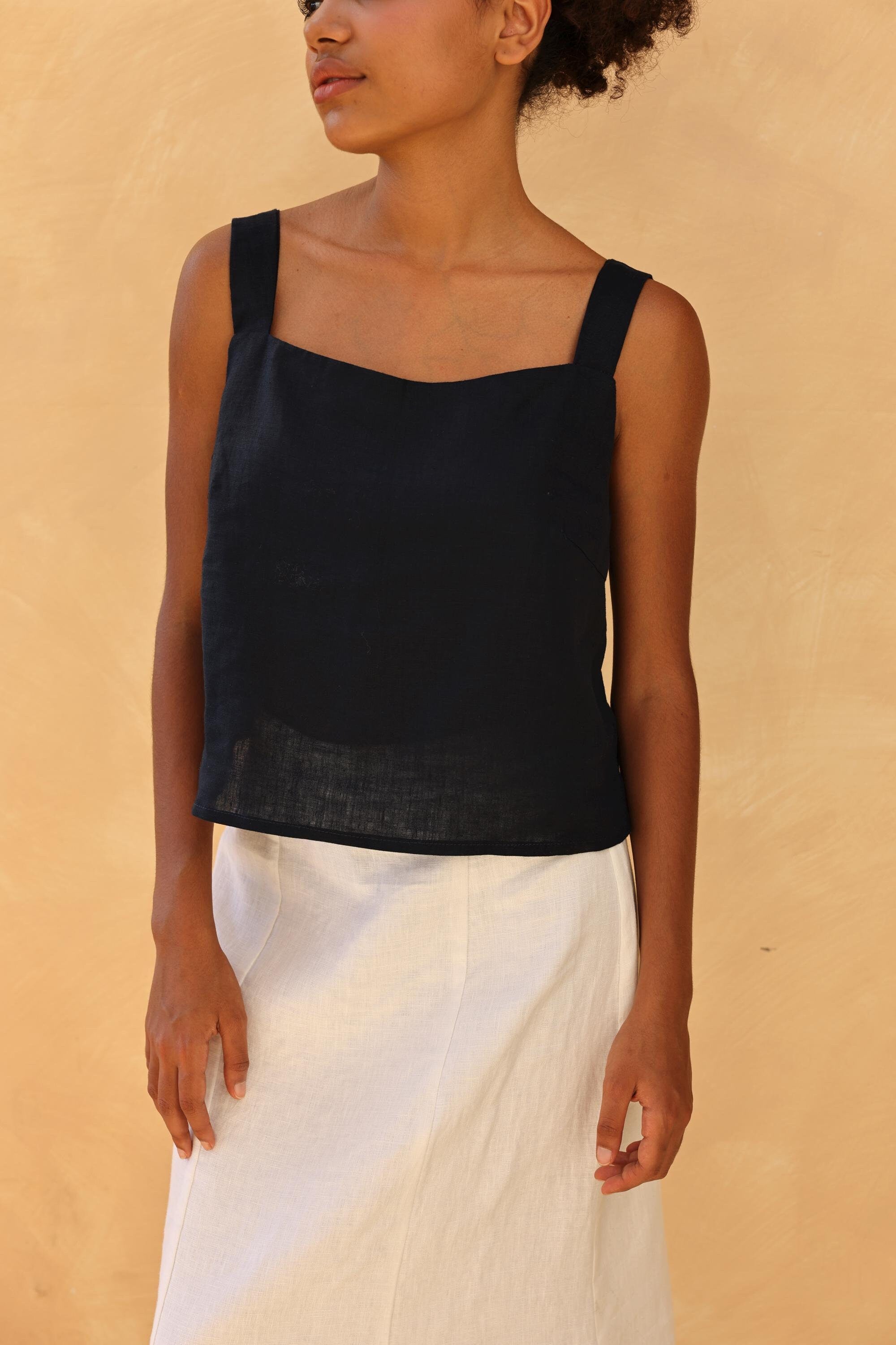 Woman wearing a black sleeveless top and white skirt against a beige background