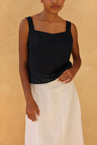 Person wearing a black sleeveless top and white skirt against a beige background