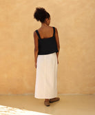 Woman wearing a black top and white skirt against a beige wall