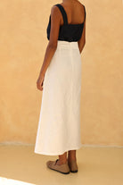 Person wearing a black top and white skirt against a beige background