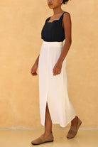 Person wearing a black top and white skirt against a beige background