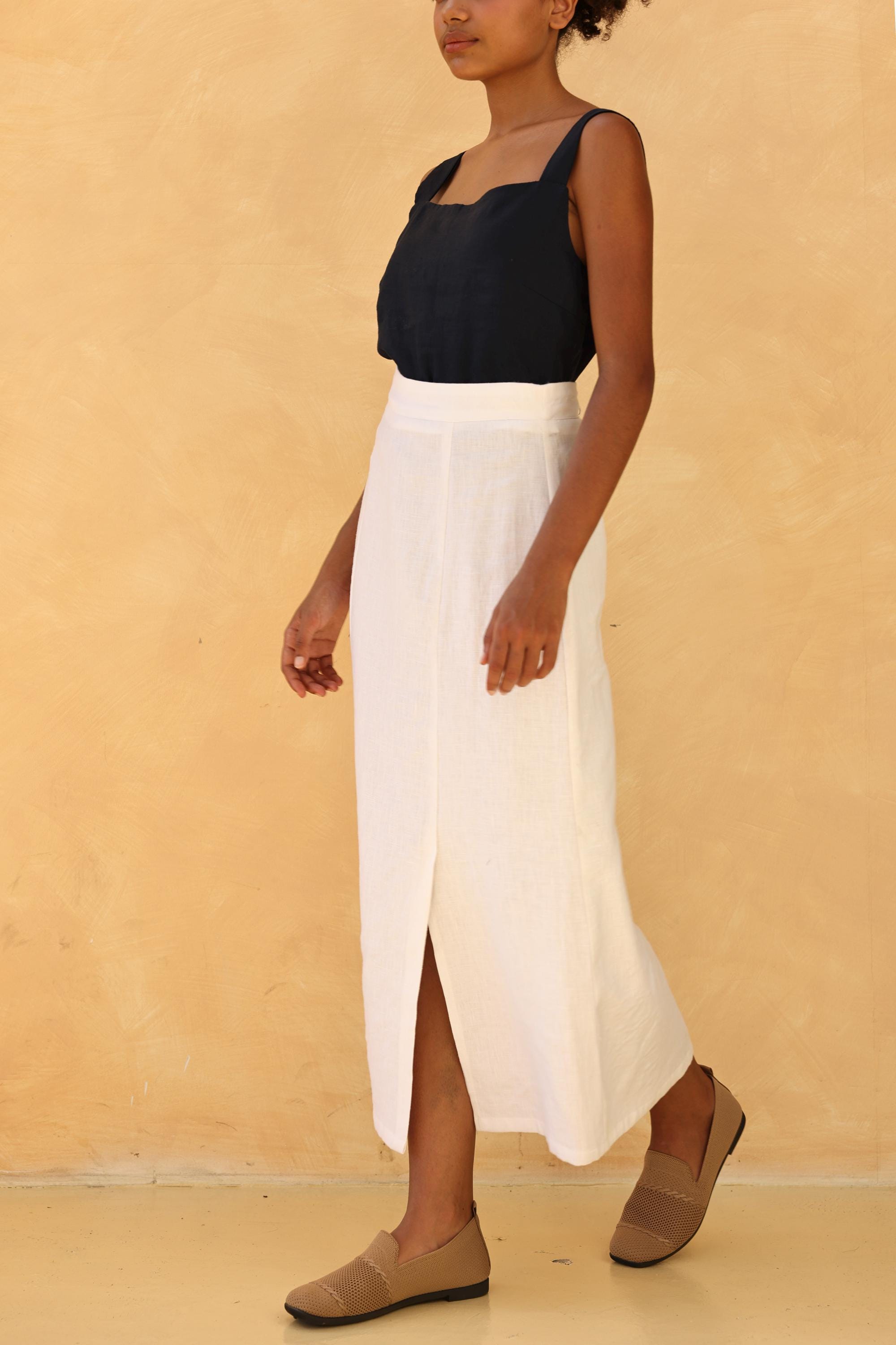 Person wearing a black top and white skirt against a beige background