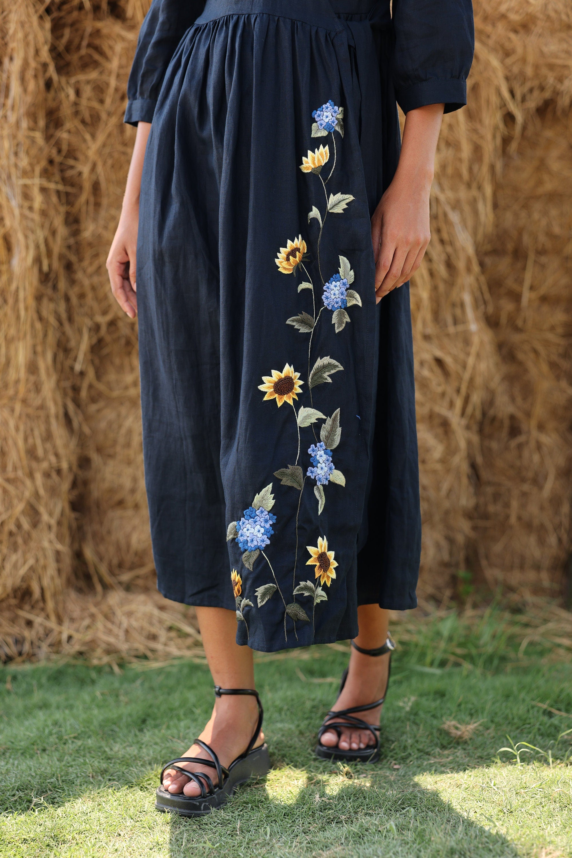 Navy blue dress with floral embroidery worn by a person, standing against a natural background.