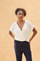 Woman wearing a white blouse and navy pants against a beige background