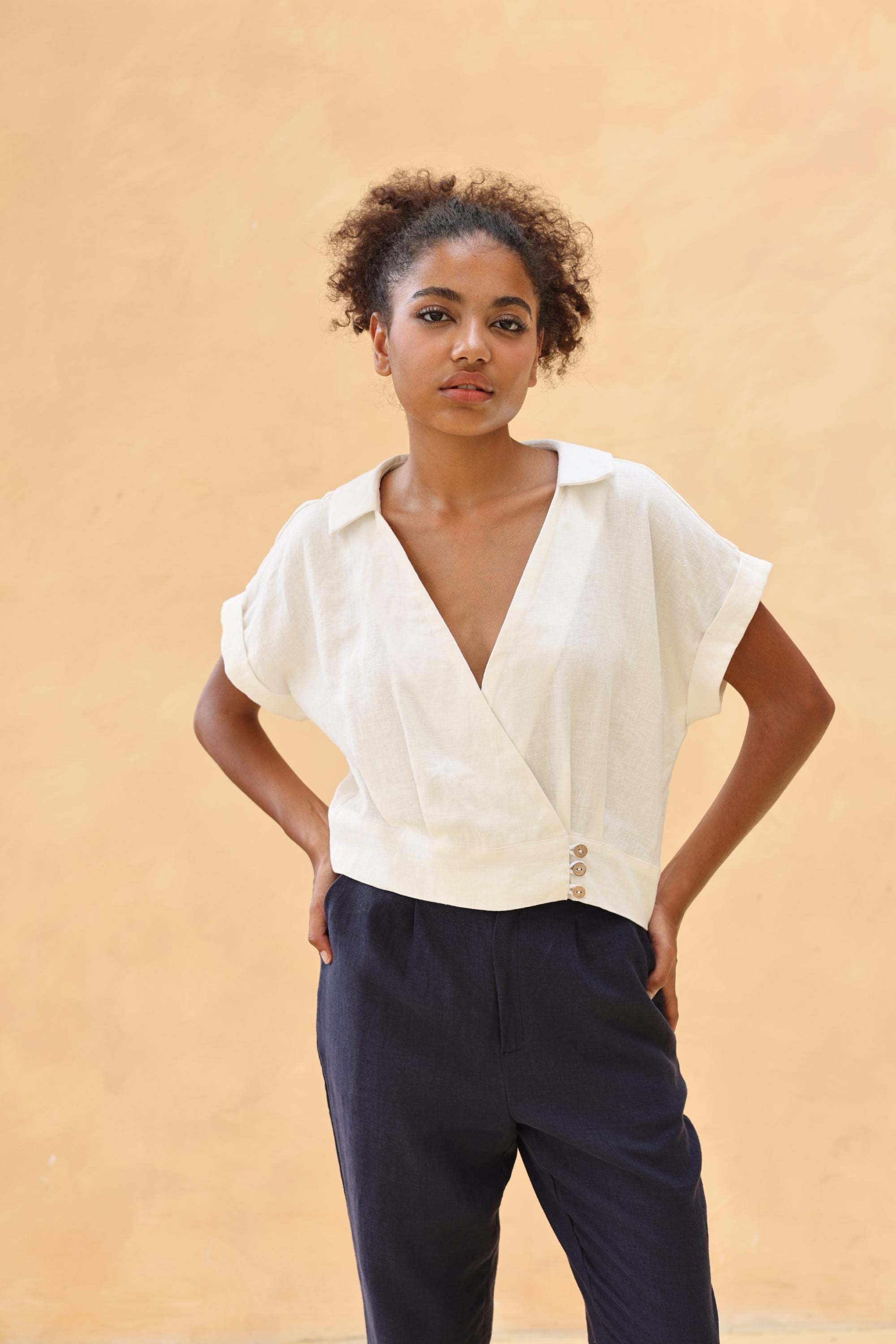 Woman wearing a white blouse and navy pants against a beige background