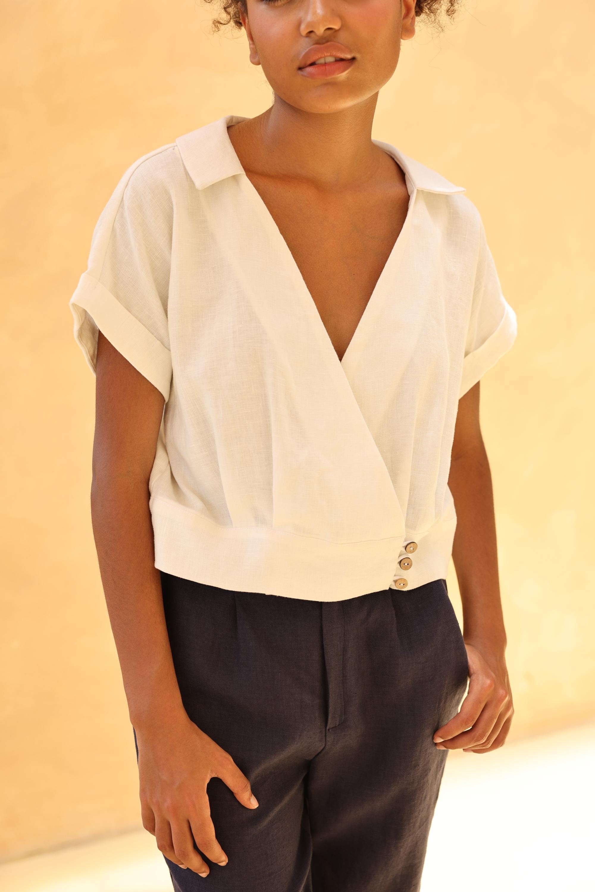 Person wearing a white blouse with short sleeves and pants against a beige background