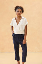 Woman wearing a white blouse and navy pants against a beige background